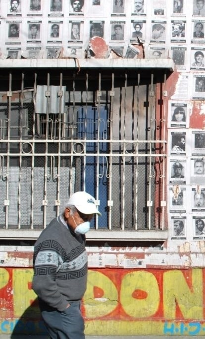 A Guatemalan man wearing a breathing masks walks in front of a wall filled with missing persons posters